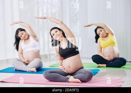 Felice bella giovane donna vietnamita seduta su tappetino yoga dentro posizione lotus e piegature laterali Foto Stock