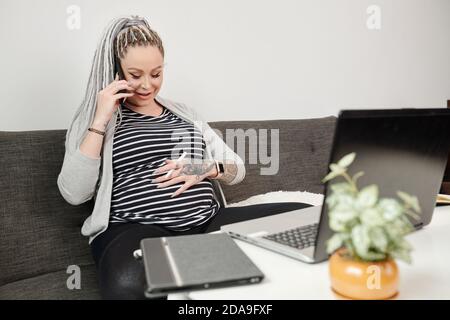 Donna incinta che prende sul telefono e che tocca la pancia sensazione che il bambino sta calciando Foto Stock