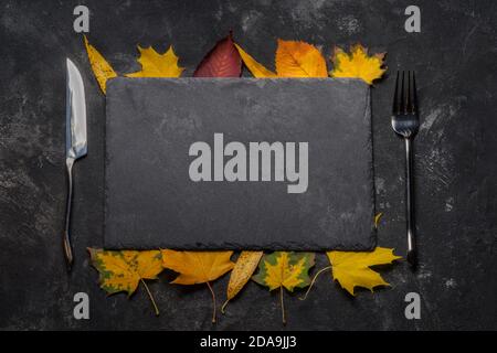 Layout autunnale con ancora vita di pietra nera vassoio, foglie autunnali, forchetta e coltello. Autunno, vista dall'alto. Foto Stock