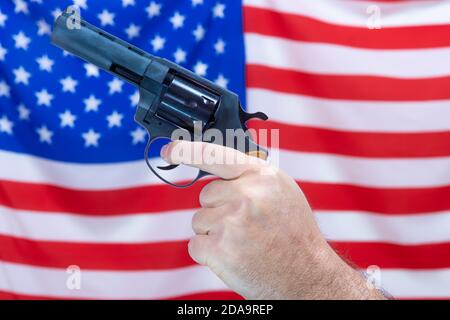 Una mano che tiene una pistola davanti ad una bandiera ondulata degli Stati Uniti d'America. Foto Stock