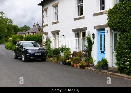 Fila di tradizionali cottage in pietra imbiancate in un pittoresco villaggio rurale, Land Rover Discovery Sport parcheggiato su strada - Linton, North Yorkshire Inghilterra UK. Foto Stock