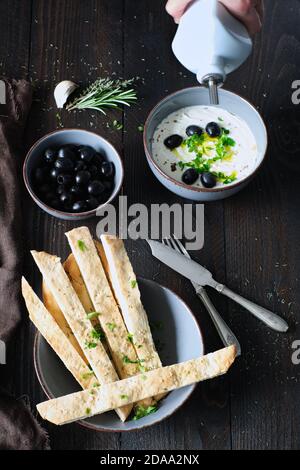 crema d'oliva fatta in casa con una ciotola di olive nere e pane naan fatto in casa, l'olio d'oliva viene versato Foto Stock