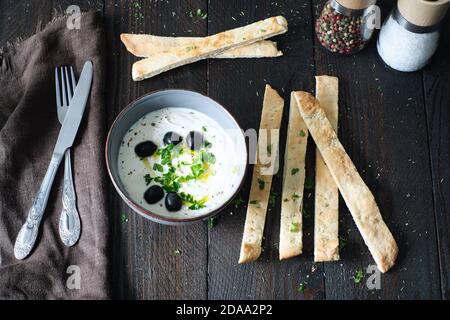 crema d'oliva fatta in casa con una ciotola di olive nere e pane naan fatto in casa, l'olio d'oliva viene versato Foto Stock