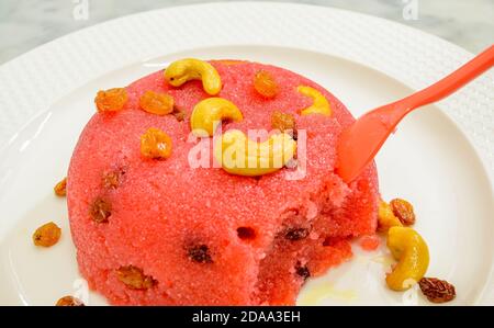 Cucchiaio rosa immerso in un piatto mezza mangiato Rava Kesari guarnito con noci di anacardi e uvetta Foto Stock