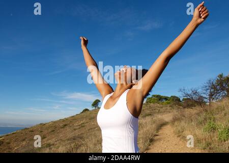 Ritratto di donna africana sopravorato in piedi all'aperto con le braccia ampio aperto e guardando verso il cielo Foto Stock