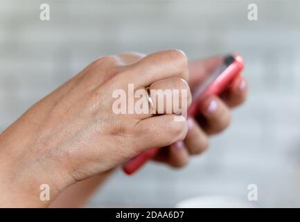 Una donna di mezza età con un anello di aggancio che tiene un telefono cellulare. Smartphone nelle mani della donna. DOF poco profondo Foto Stock