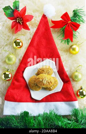 Cappello di Babbo Natale, ornamenti di Natale e un piatto con dolci greci di Natale, melomakarona Foto Stock