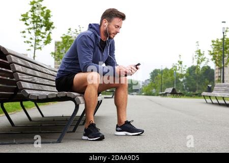 Ritratto a tutto corpo di un atleta anziano seduto in ascolto di musica esterno Foto Stock