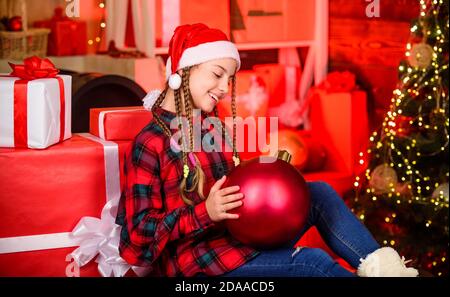 Piccola ragazza carina con grande albero di natale della palla. Spirito di Natale. Negozio di arredamento. Colore preferito. Stile rosso. Diffondere l'amore. Vacanze invernali. Concetto di Natale. Bambini Fancy babbo natale Godetevi la celebrazione del nuovo anno. Foto Stock