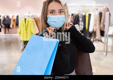 Donna come cliente con una maschera a causa di Covid-19 pandemia mentre lo shopping con un sacco di borse Foto Stock