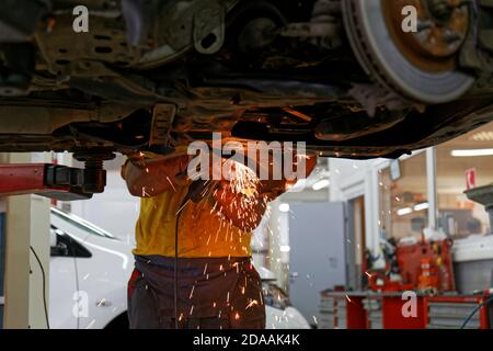 Il tecnico del servizio di assistenza auto pulisce le vecchie parti metalliche dalla ruggine utilizzando una smerigliatrice angolare. Le scintille volano in direzioni diverse. Foto Stock