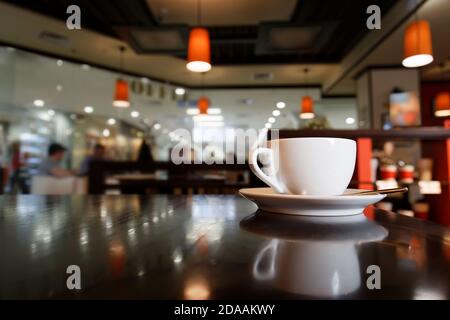 Tazza di caffè bianca sul tavolo nella caffetteria su sfondo sfocato Foto Stock