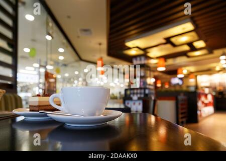 XJtazza bianca di caffè sul tavolo nella caffetteria su sfondo sfocato Foto Stock