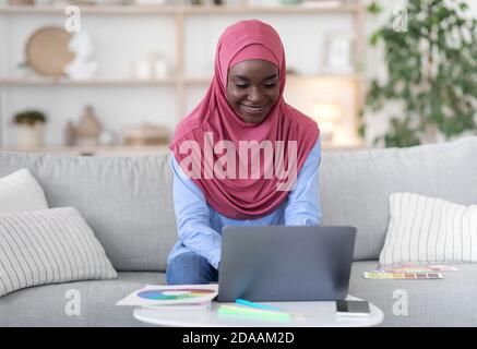 Corsi di Design online. Giovane musulmana africana che studia con il laptop a casa Foto Stock