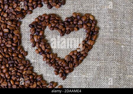 I chicchi di caffè arrostiti a forma di cuore sono sparso su burlap Foto Stock