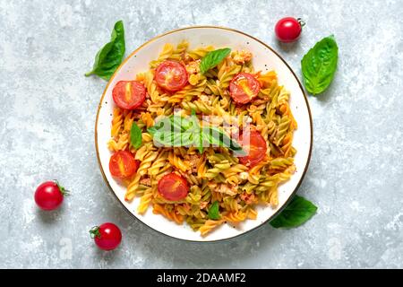 Fusilli - classica pasta italiana di grano duro con carne di pollo, pomodori ciliegia, basilico in salsa di pomodoro in ciotola bianca su tavola grigia in cemento Foto Stock