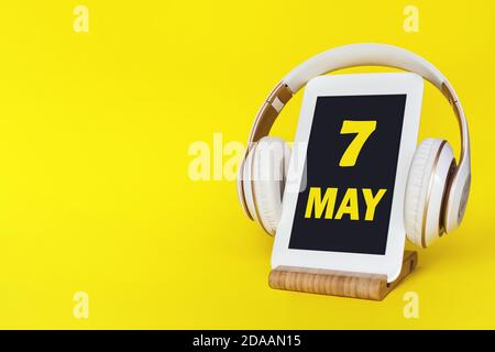 7 maggio. Giorno 7 del mese, data del calendario. Cuffie eleganti e moderno tablet su sfondo giallo. Spazio per il testo. Formazione concettuale, tecnologia, vita Foto Stock