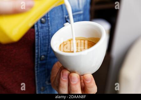 Tazza per closeup di cappuccino in mano al barista che versa il latte per fare la latte art. Poco profonda messa a fuoco.