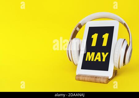 11 maggio . Giorno 11 del mese, data del calendario. Cuffie eleganti e moderno tablet su sfondo giallo. Spazio per il testo. Formazione concettuale, tecnologia, l Foto Stock