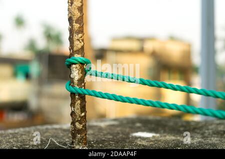 Una corda è legata in un nodo intorno a un palo di recinzione, corda legata attacco nodi su un palo di ferro arrugginito isolato da sfondo. Foto Stock