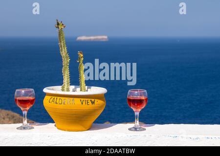 Bicchieri di vino rosso con vista sul mare blu sull'isola di Santorini in Grecia. L'iscrizione sul piatto in inglese, vista caldera. Foto Stock