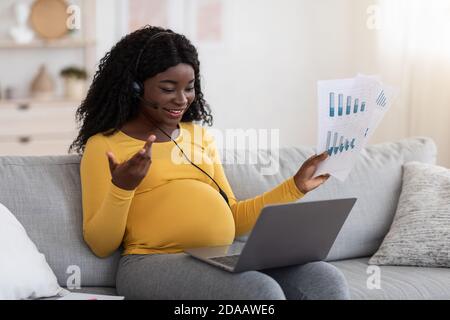 Donna incinta nera freelance che ha videoconferenza Foto Stock