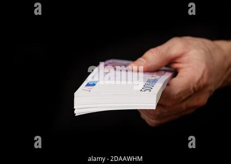 Closeup di una mano mans che tiene un pacco di banconote in euro isolato su sfondo nero. Messa a fuoco superficiale. Foto Stock