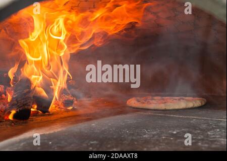 Pizza italiana che sta cucinando in un forno a legna Foto Stock