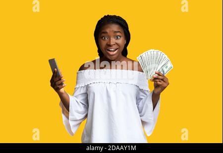 Concetto di cashback. Smartphone di Young Woman Holding e Dollar Cash eccitati Foto Stock