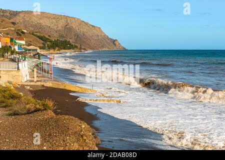 Il mare è ruvido, il vento soffia, le onde si ondano su una spiaggia rocciosa deserta e si schiumano . Foto Stock