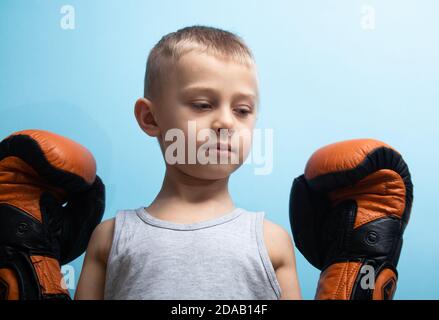 Un ragazzo in Guanti Boxing è impegnato in Boxing. Il concetto di parenting sano e sport. Bambino su sfondo blu Foto Stock