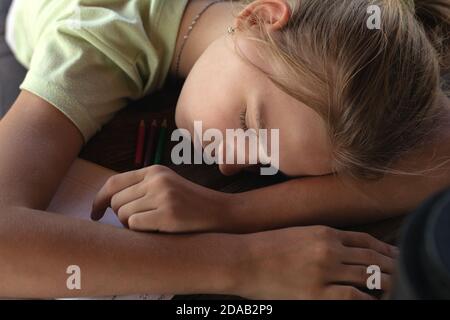 La giovane ragazza stanca si addormentò facendo noiose esercitazioni scolastiche. La bambina scolastica esausta dorme alla scrivania, sdraiata sui quaderni. Foto Stock