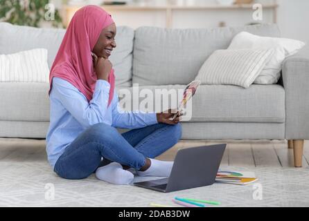 Black Muslim Female Graphic Designer lavora a distanza a casa, tenendo campioni di colore Foto Stock