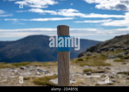 Pietra miliare che segna la strada su un percorso di montagna in una giornata di sole. Cairn di legno. Foto Stock