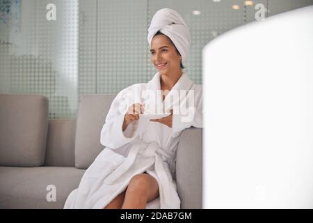 Cliente seduto su un divano che riposa in un bianco accappatoio e asciugamano Foto Stock