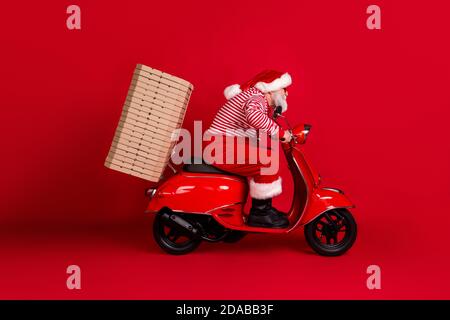 Foto del profilo a lunghezza intera di un'autostrada in pensione con scooter nonno consegna immediata pizza indossare santa x-mas costume sospetti stivali da sole a strisce Foto Stock