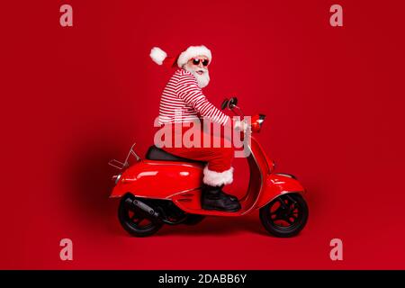 Foto del profilo a lunghezza intera di un'autostrada in pensione con scooter nonno road veloce spensierato indossare santa x-mas costume sospetti stivali da sole camicia a righe Foto Stock