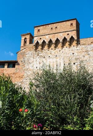 Frammento del muro della fortezza con una torre difensiva e il campanile di San Gimignano, Italia Foto Stock