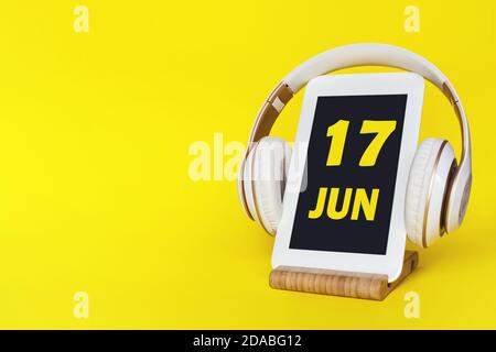 17 giugno. Giorno 17 del mese, data del calendario. Cuffie eleganti e moderno tablet su sfondo giallo. Spazio per il testo. Istruzione, tecnologia, stile di vita Foto Stock