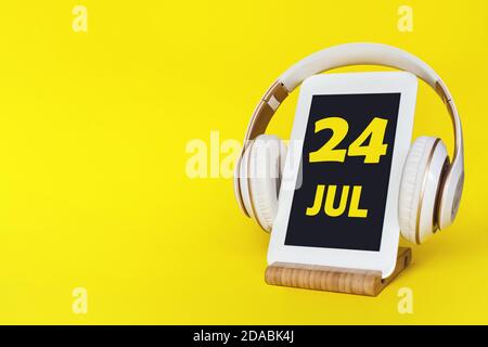 24 luglio. Giorno 24 del mese, data del calendario. Cuffie eleganti e moderno tablet su sfondo giallo. Spazio per il testo. Istruzione, tecnologia, stile di vita Foto Stock