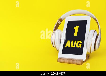 1 agosto . Giorno 1 del mese, data del calendario. Cuffie eleganti e moderno tablet su sfondo giallo. Spazio per il testo. Istruzione, tecnologia, stile di vita Foto Stock