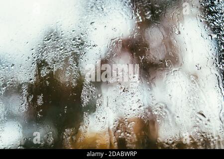 Riflesso offuscato della strada in una finestra appannata, gocce d'acqua dopo la pioggia scorrono sul vetro. Gocce d'acqua sulla finestra. Concetto di umore piovoso. Foto Stock