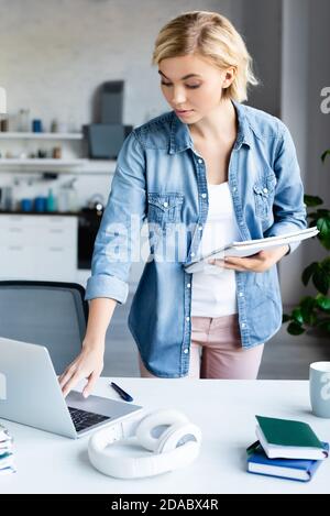 giovane donna bionda che tiene il taccuino e studia da casa Foto Stock