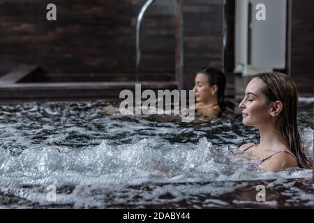 Vista laterale della donna con occhi chiusi seduti vasca idromassaggio e acqua gorgogliante mentre ti rilassi nel centro benessere centro Foto Stock