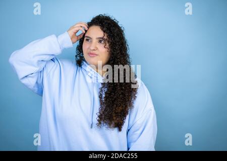 Giovane bella donna che indossa felpa casual su sfondo blu isolato confondere e meraviglia circa domanda. Incerto con dubbio, pensando con h Foto Stock