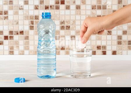 La mano della donna è pronta a far cadere la pillola di vitamina effervescente solubile in un bicchiere di acqua potabile pura. Vitamine e integratori alimentari. Dissetarsi Foto Stock