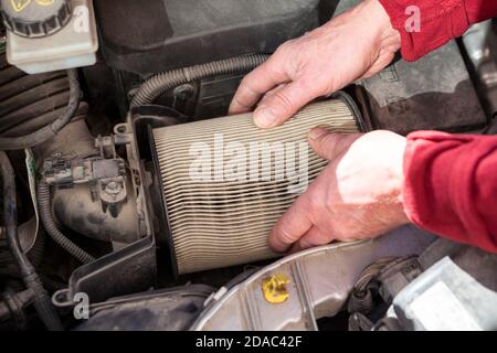 Mani meccaniche che estrano la cartuccia d'aria sporca dall'airbox del motore dell'auto, vista ravvicinata Foto Stock