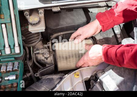 Mani meccaniche che estrano la cartuccia di carta sporca del filtro dell'aria dalla scatola dell'aria del motore dell'automobile, vista ravvicinata Foto Stock