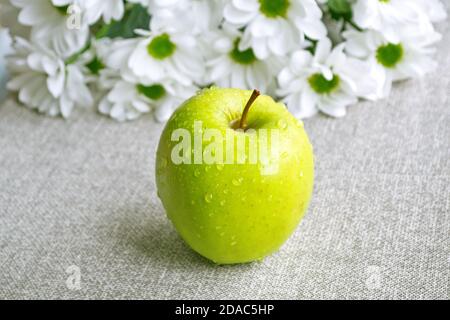 Una mela verde lavata ("Golden") sul tavolo. Fiori bianchi sullo sfondo. Foto Stock