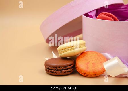 Quattro Macaron francesi dai colori vivaci con scatola di cartone rosa su sfondo di pesca. Foto Stock
